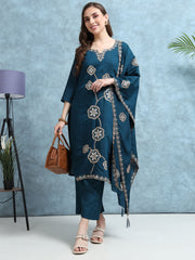 Woman wearing a blue embroidered outfit holding a brown handbag against a light blue background